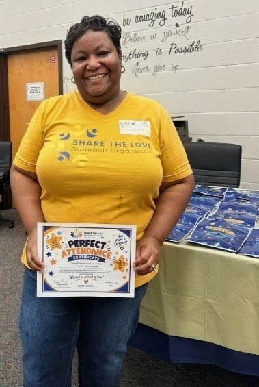 A Share the Love volunteer proudly holding a Perfect Attendance Certificate at Sanders Elementary