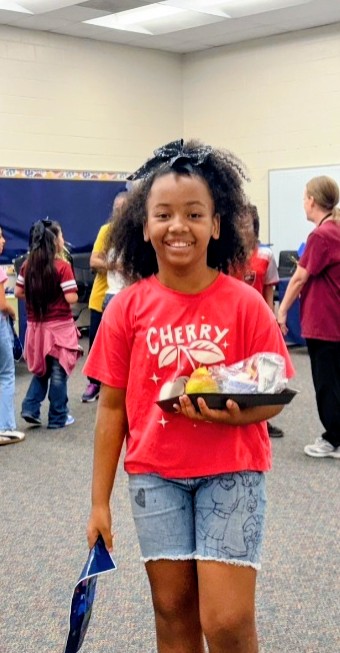 A Sanders Elementary student smiling while holding her special pizza lunch and goodie bag