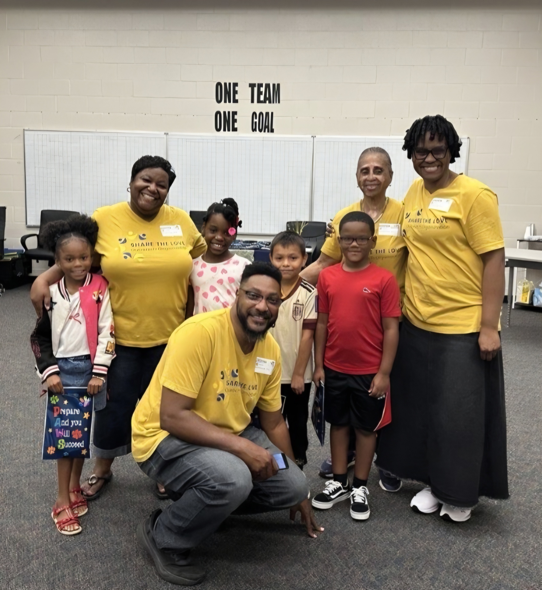 Share the Love volunteers posing with Sanders Elementary students under the One Team One Goal banner